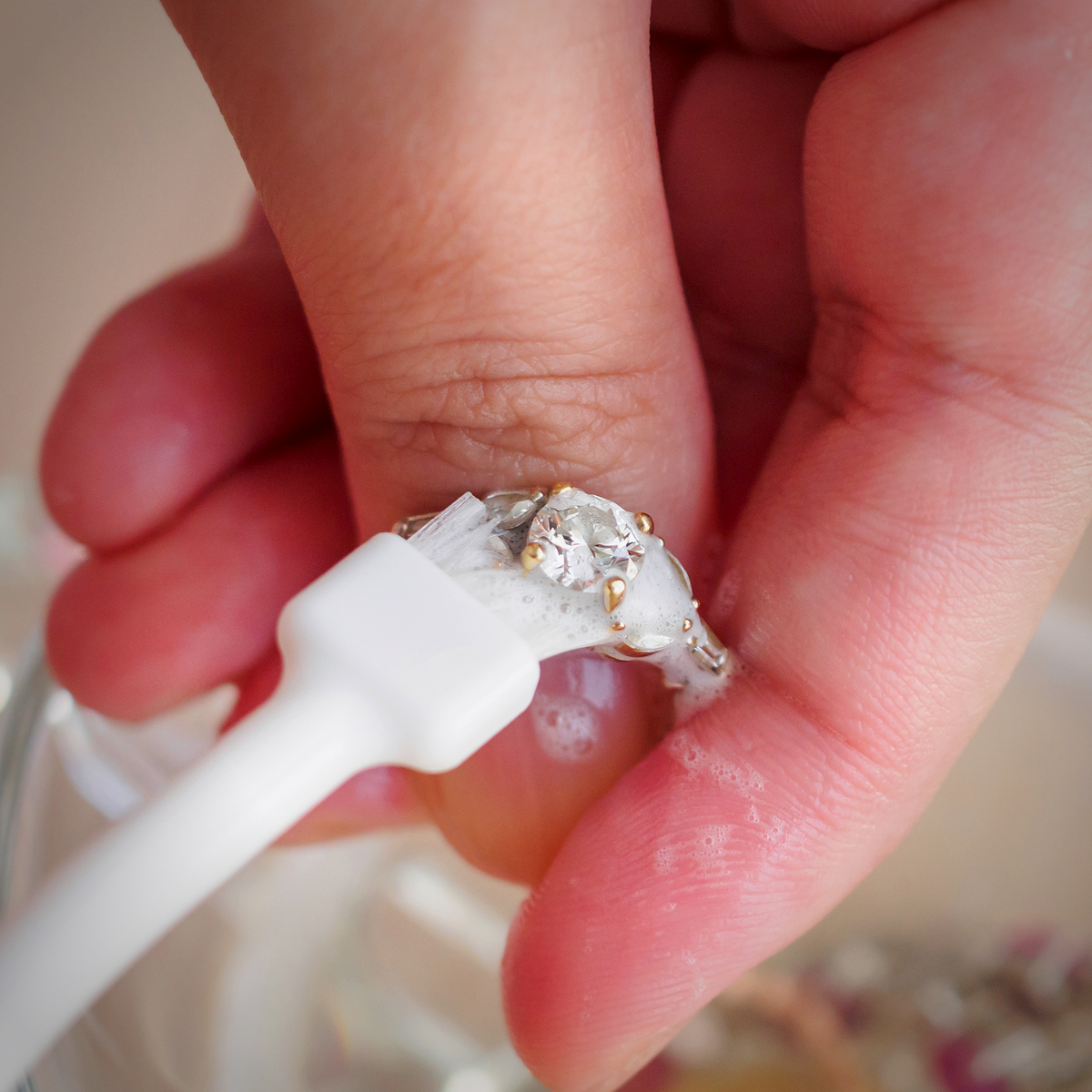 Cleaning a diamond engagement ring in soapy water with a soft white brush