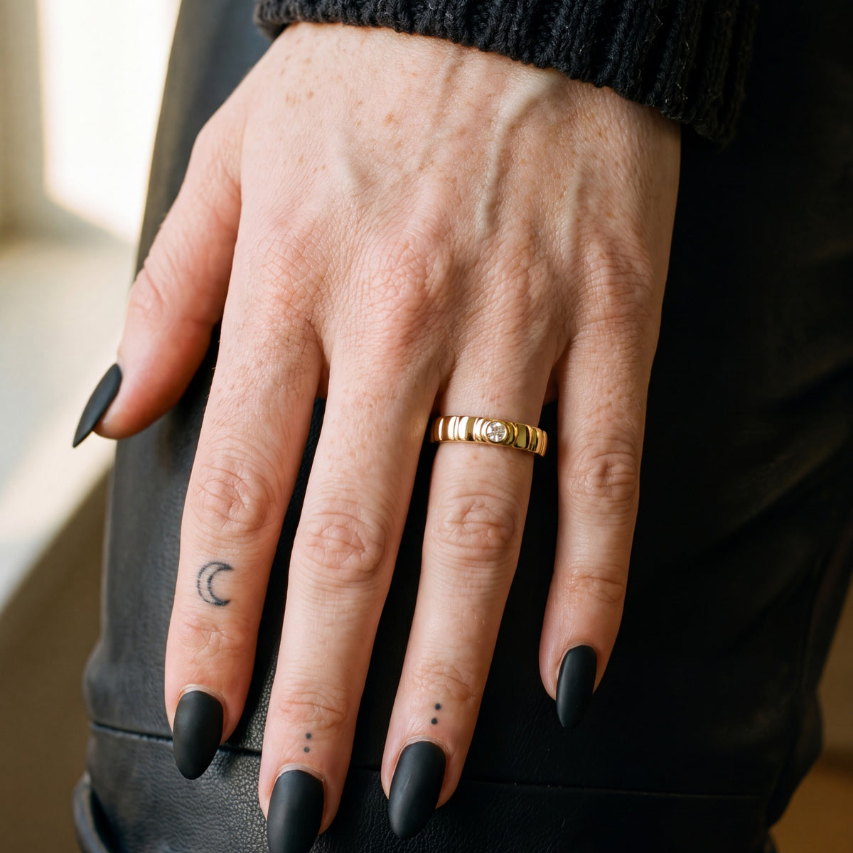 Gravitational Wave white diamond wedding band in yellow gold worn on the hand, black leather trousers