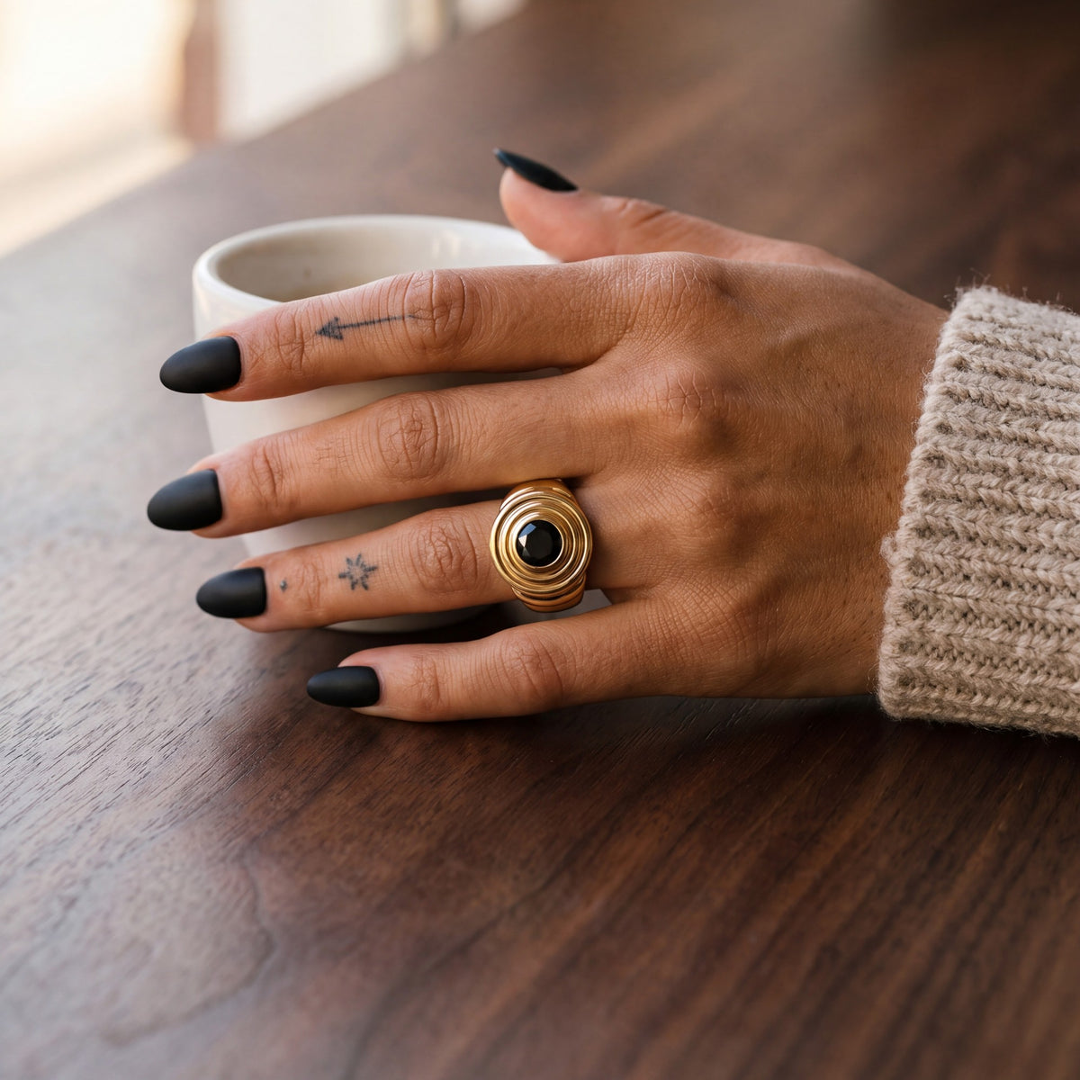 Gravitational Wave black diamond engagement ring in yellow gold worn on the hand, cafe table with an espresso cup