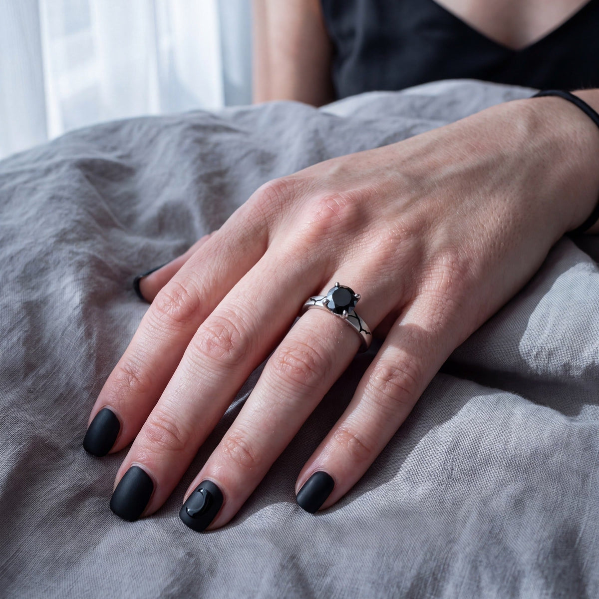 Kintsugi black diamond engagement ring in white gold, the black enamel crack across the band, worn on the hand on grey linen