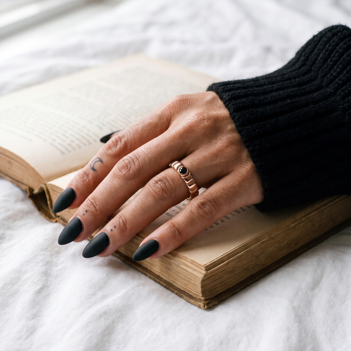 Rose gold Gravitational Wave wedding band with a black diamond on a hand resting on an open book