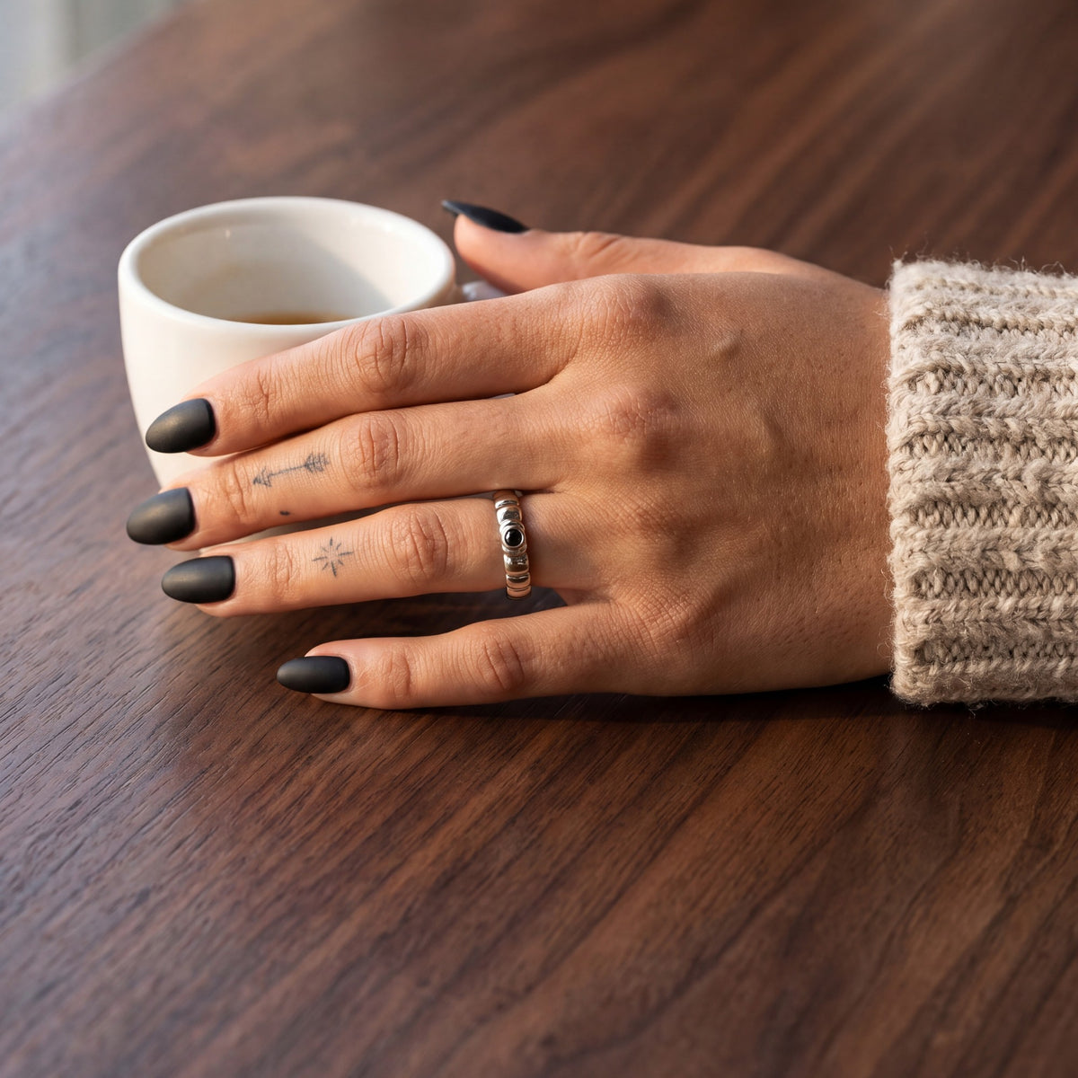 White gold Gravitational Wave wedding band with a black diamond on a hand on a walnut cafe table