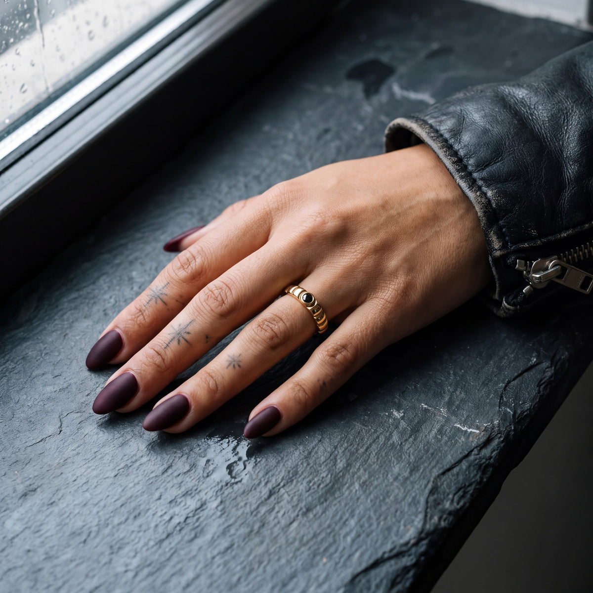 Gravitational Wave black diamond wedding band in yellow gold worn on the hand, slate windowsill, leather jacket