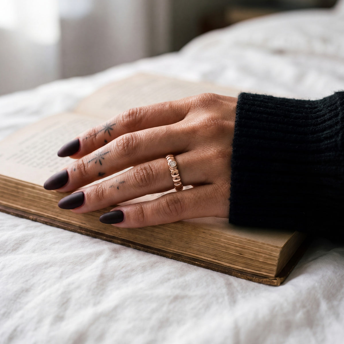 Rose gold Gravitational Wave wedding band with a white diamond on a hand resting on an open book