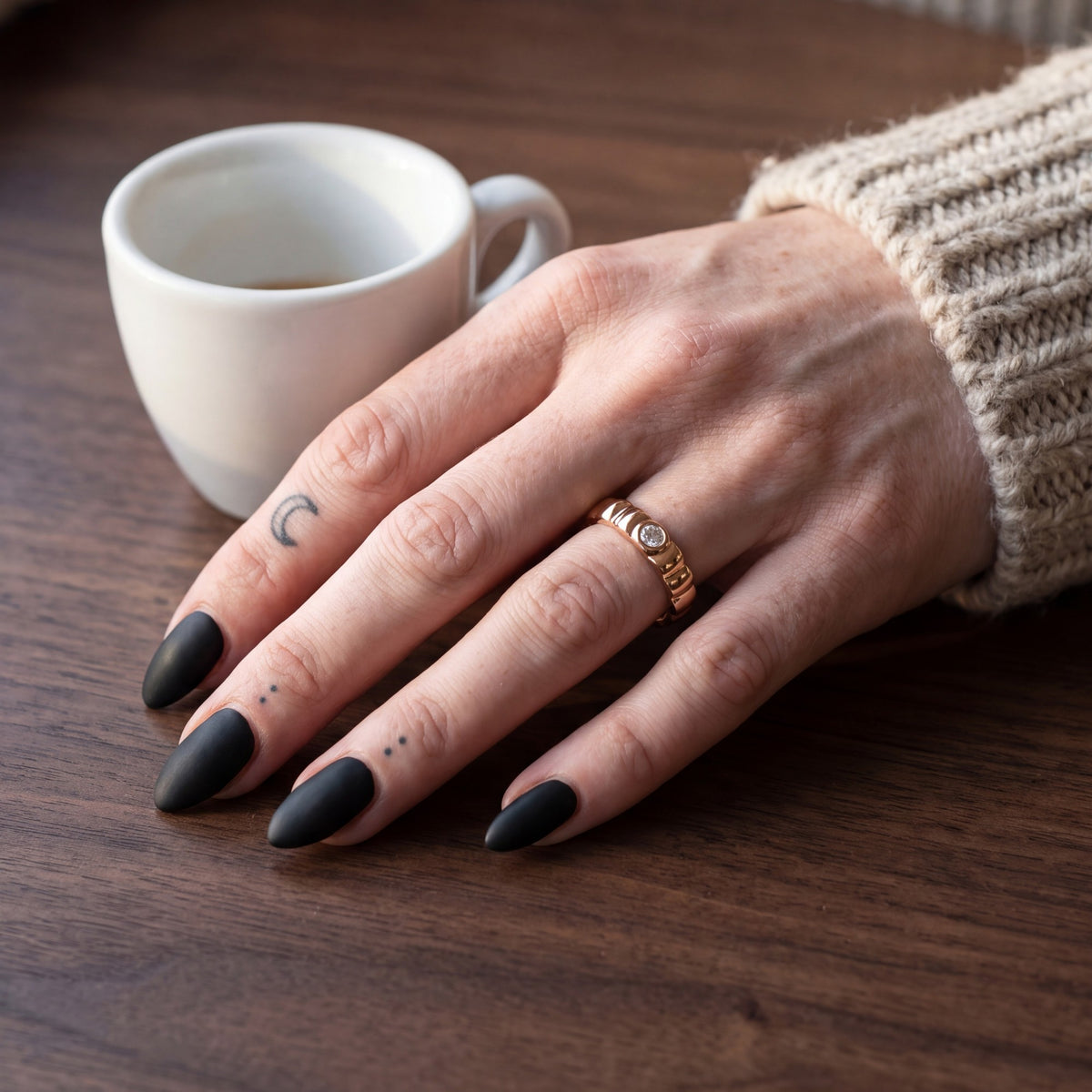 Rose gold Gravitational Wave band with a white diamond on a hand on a walnut cafe table