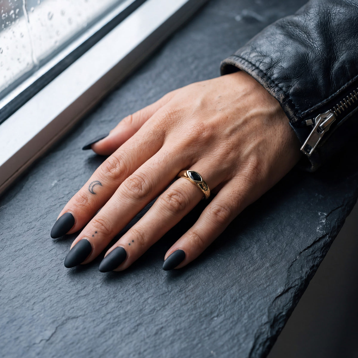 Disturbed marquise black diamond engagement ring in yellow gold worn on the hand, slate windowsill