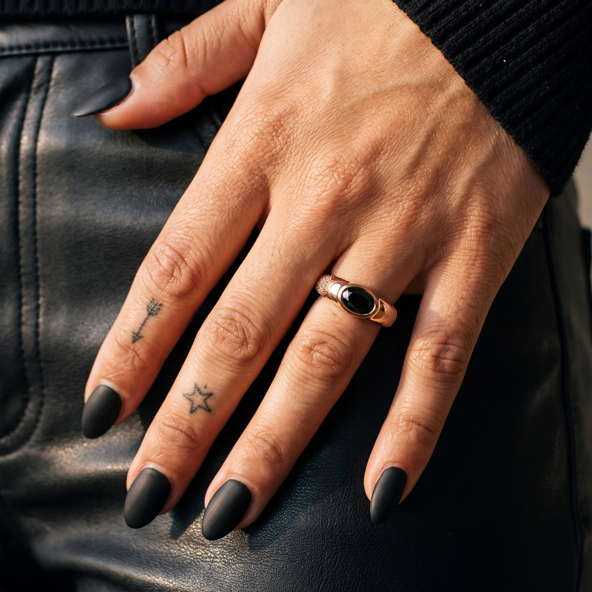 Rose gold Smoothen east-west oval black diamond ring on a hand resting on black leather trousers