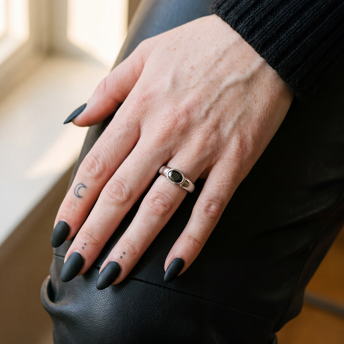 White gold Smoothen oval black diamond ring on a hand resting on black leather trousers