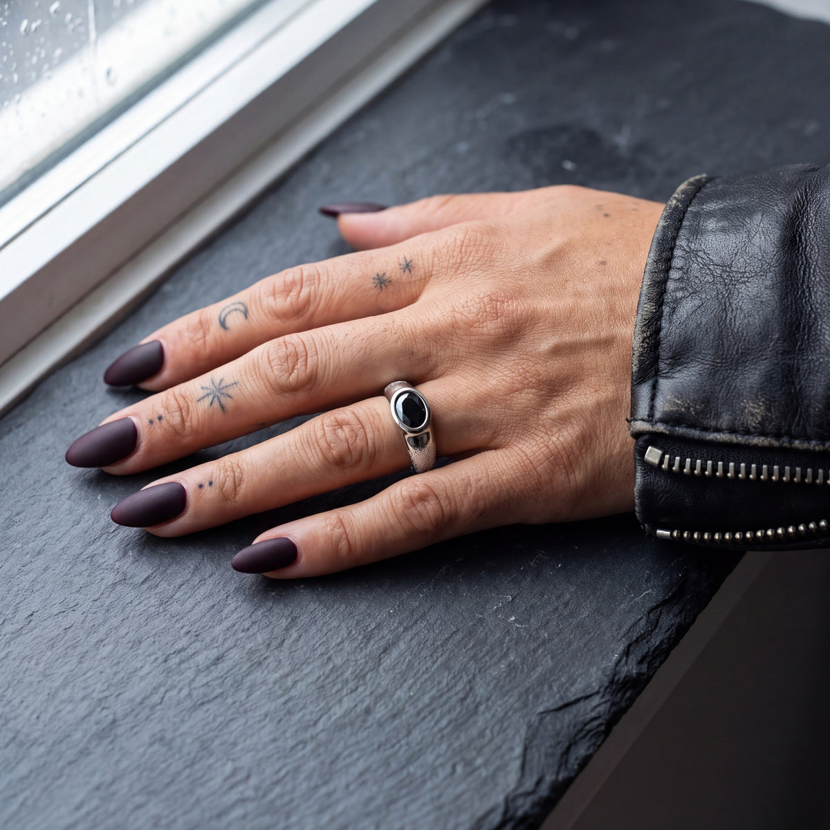 White gold Smoothen black diamond ring on a hand on a slate windowsill, black leather jacket