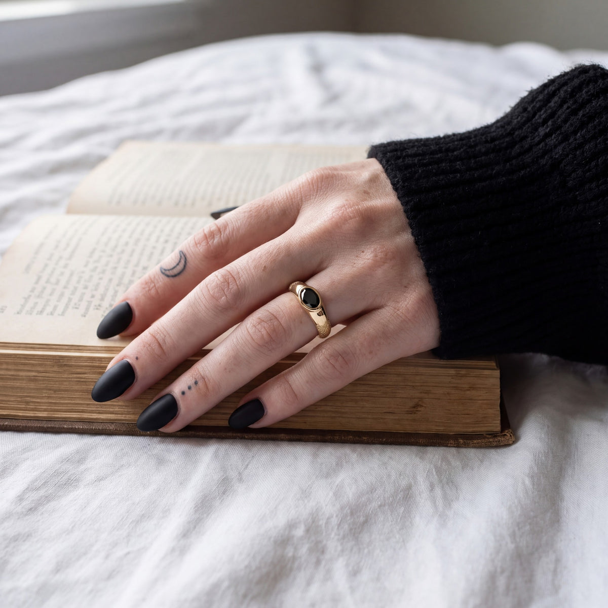 Smoothen oval black diamond engagement ring in yellow gold worn on the hand, resting on an open book