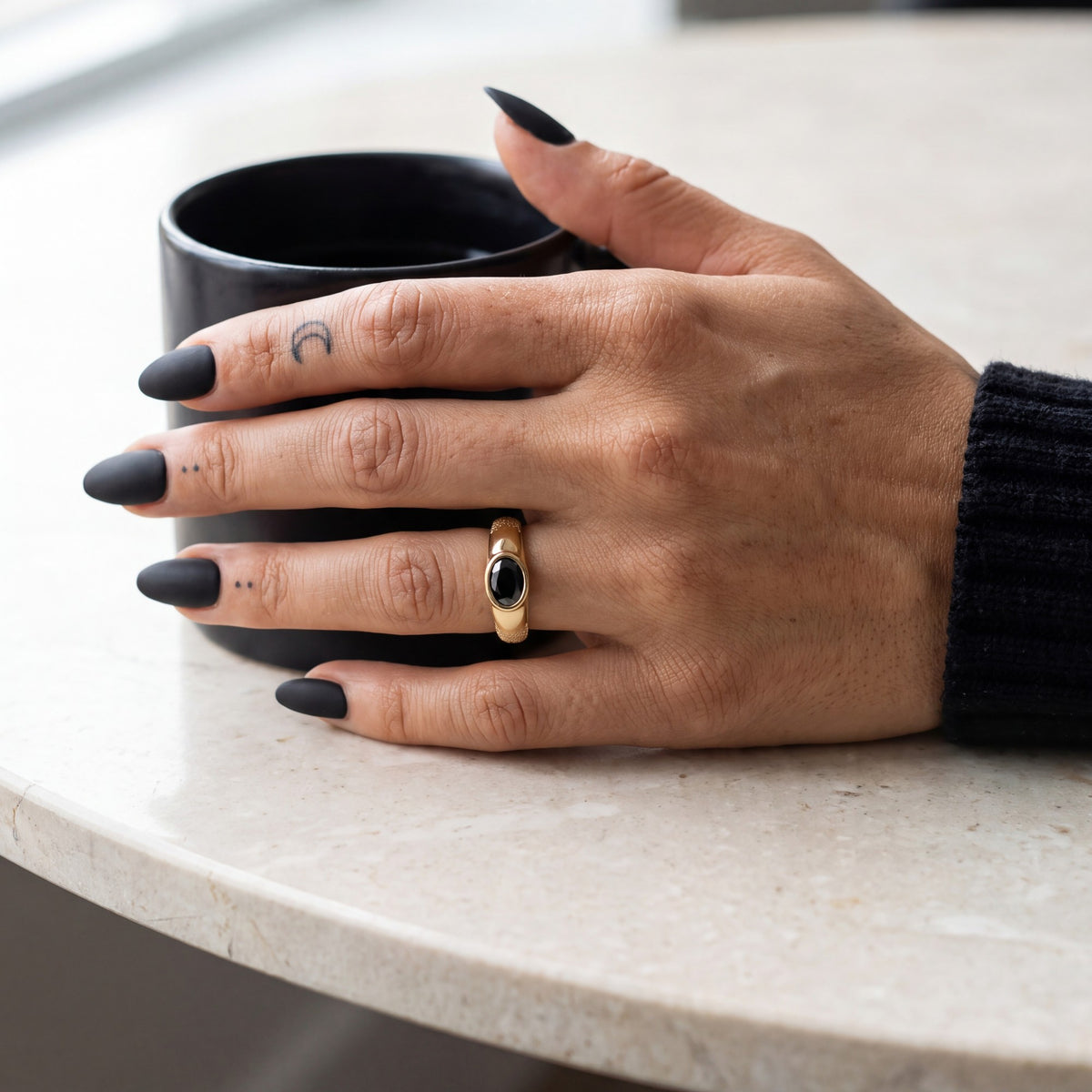 Yellow gold Smoothen oval black diamond ring on a hand beside a black coffee mug