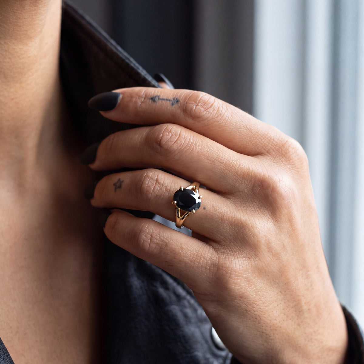 Melusine oval natural black diamond split shank ring in yellow gold, her hand at a leather jacket collar