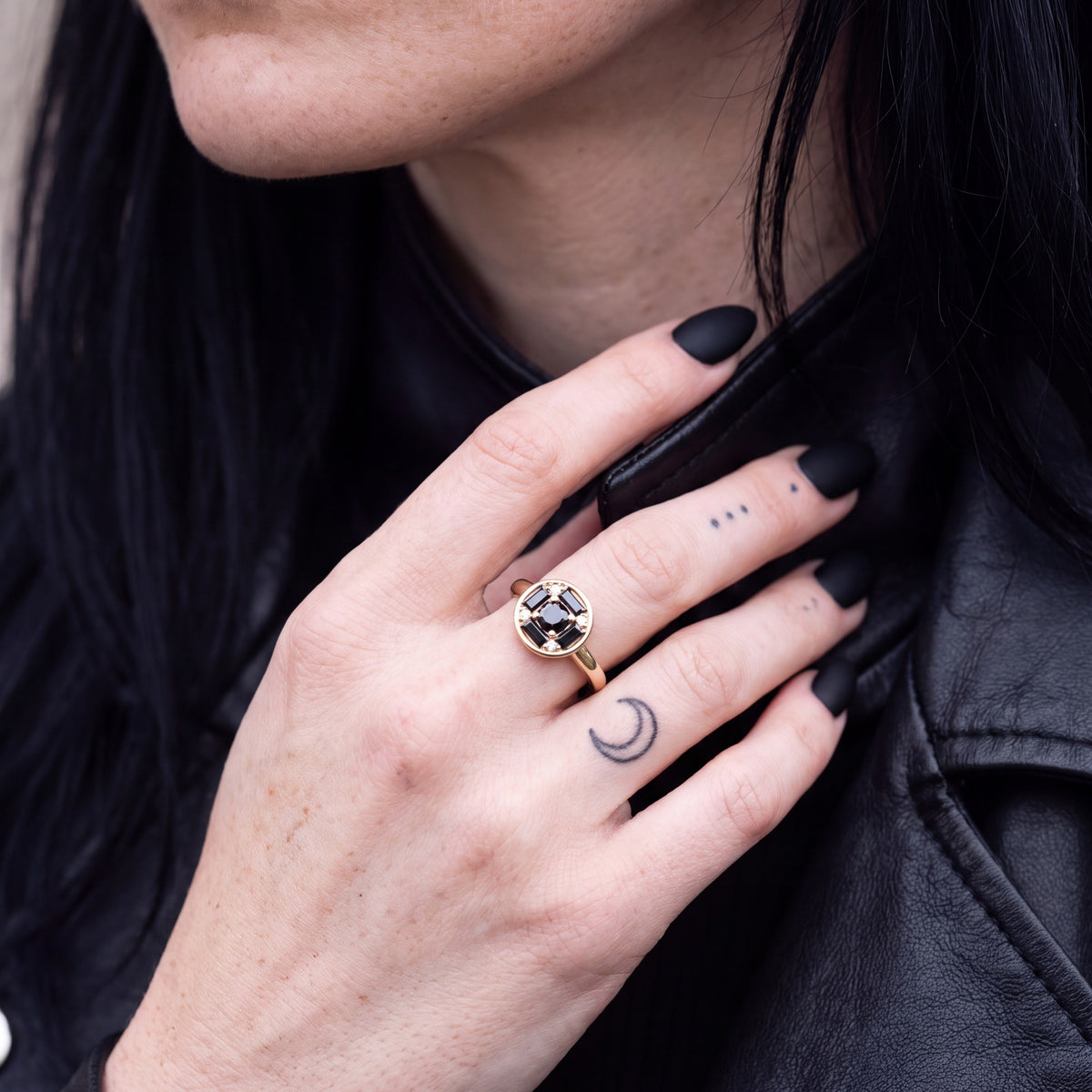 Polaris compass natural black diamond ring in yellow gold, her hand at the collar of a leather jacket