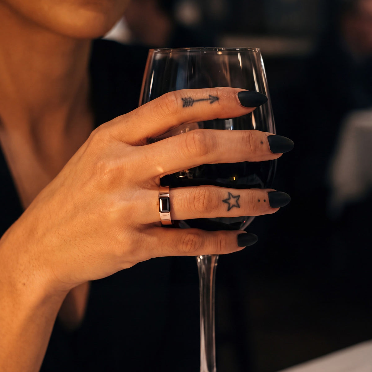 Janus east-west baguette natural black diamond ring in rose gold, holding a glass of red wine
